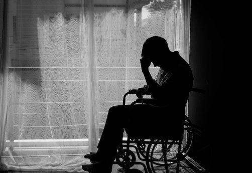 Silhouette of handicapped Man sitting on wheelchair in front of a large panoramic window in hospital,He is sad and lonely-Black and white tone