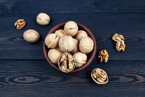 Walnut kernels in a bowl on a dark wooden background.