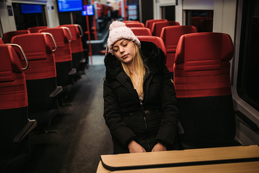 Beautiful young blond woman in winter coat and knit hat sleeping in subway train on cold winter night
