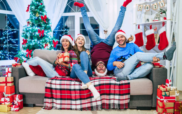 Excited and laughing group young best friends are celebrating the Christmas holidays in a decorated home with a big bright Christmas tree in the background Excited and laughing group young best friends are celebrating the Christmas holidays in a decorated home with a big bright Christmas tree in the background december 31 stock pictures, royalty-free photos & images
