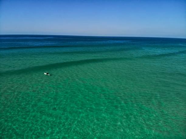 ein einsamer surfer saß auf einem longboard im türkisfarbenen wasser des fistral beach, newquay - tide aerial view wave uk stock-fotos und bilder
