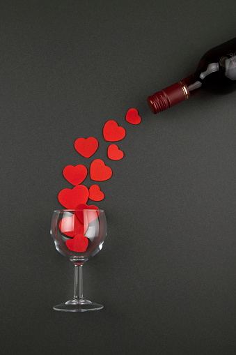 Glass with hearts and wine bottle on black background