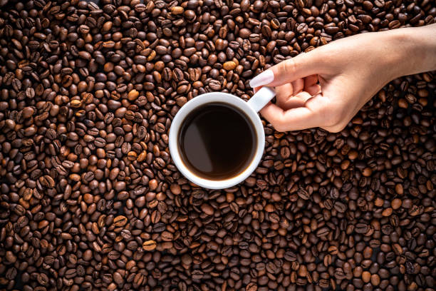 Female hand holding black coffee cup with long nails on coffee beans medium toast background