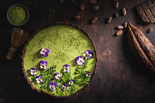 Matcha tea and chocolate superfood tart with moringa leaves nuts and edible pansy flowers with cocoa pod and beans