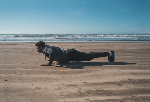 Portrait of an athletic man doing push-ups at the beach. Sport and healthy lifestyle concept.