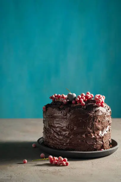 Chocolate cake with red currant frozen berries on top and cutting knife vintage on blue background