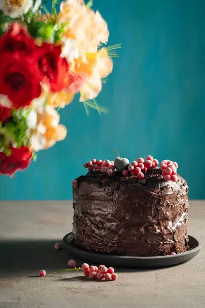 Chocolate cake with red currant frozen berries on top and blurred flowers on blue background