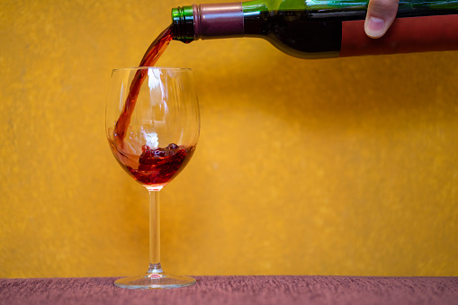 Red wine pouring in a glass on yellow background