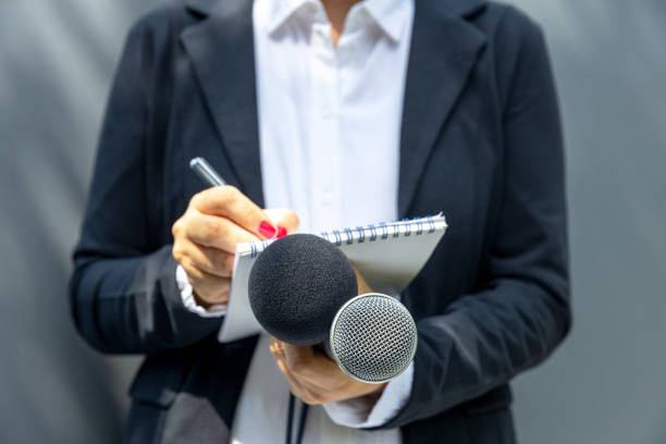 istock Female journalist at media event or press conference, writing notes, holding microphone. Journalism concept. 1278624633