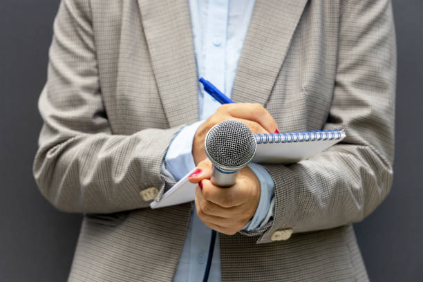 istock Female journalist at media event or press conference, writing notes, holding microphone. Journalism concept. 1278626354