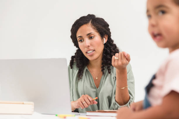 istock Working mom gestures while video conferencing; daughter colors 1278631104