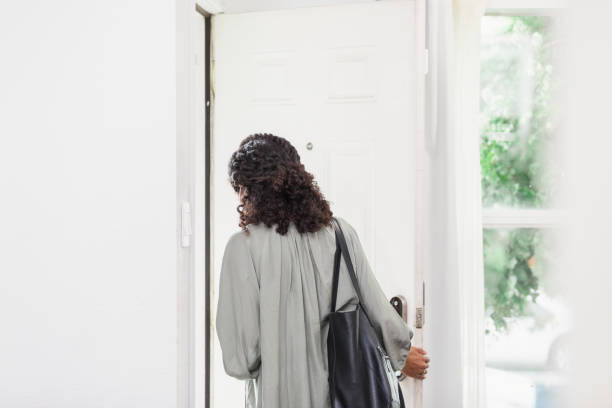 Unrecognizable young adult woman leaves house carrying purse The unrecognizable young adult woman leaves her house carrying a purse.  She is leaving through the front door. people walking away stock pictures, royalty-free photos & images