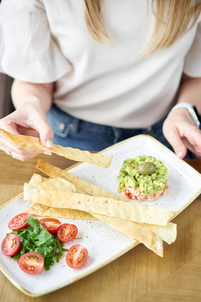 la donna mangia granchio da insalata, avocado, olio di agrumi, spezie. carne di granchio con matzo su piatto bianco per frutti di mare cotti. - cooking close up matzo food foto e immagini stock