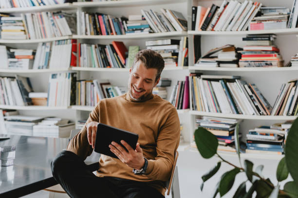 istock Smiling Handsome Freelance Businessman Using a Digital Tablet in his Office/ Library 1278645182
