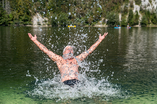 Cheerful senior men splashing and jumping in green lake water in Lake Bohinj.