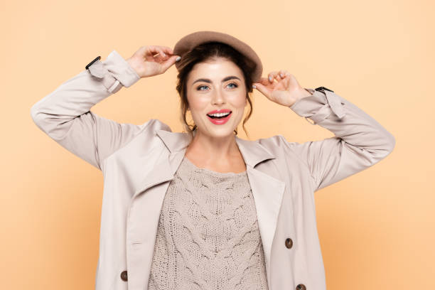 istock stylish woman in trench coat touching beret while looking away on peach 1278653665