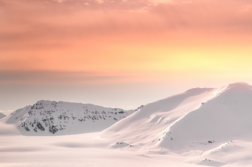 Snow-covered mountains of Svalbard at dusk. During the summer months the sun falls low in the sky but never sets, casting a warm glow across the landscape.