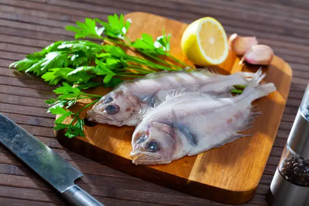 Uncooked roosterfish with greens and garlic on wooden board before cooking