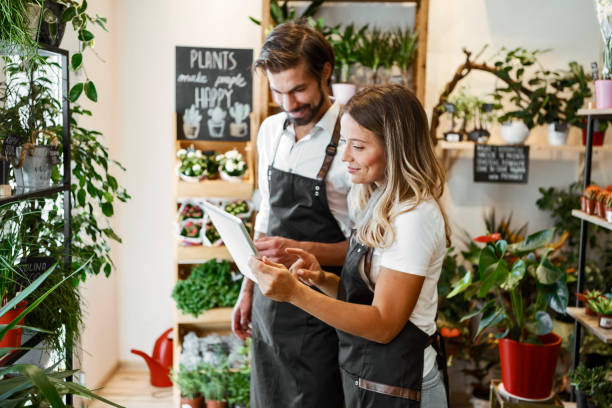 デジタルタブレット上の植物をチェックする独自の花屋で働く - florist small business flower shop owner ストックフォトと画像