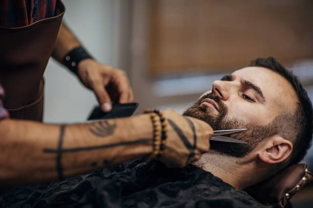 istock Close up of a barber styling client's beard with scissors 1278664076