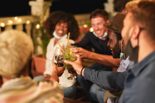 istock Happy multiracial people cheering with drinks while wearing surgical face mask under chin - Concept of private party at home because of coronavirus 1278664150