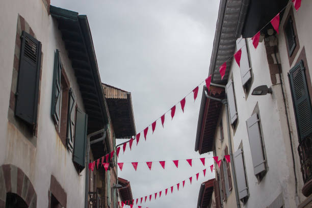 istock Red triangle flags between medieval buildings. Fiesta concept. Festive decoration on the streets of ancient town in Europe. Red flags on rope on house facade. 1278667453