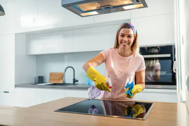 Worthy cheerful housewife with rubber gloves spraying stove and cleaning it with sanitizer.