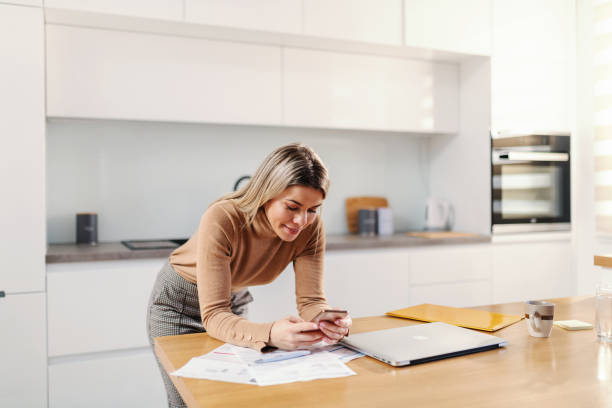 istock Young attractive blond woman leaning on kitchen table and using smart phone for e-banking. 1278667686