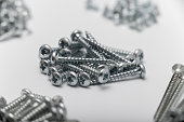 Self-tapping screws of various types are sorted into several piles. Shallow depth-of-field photograph with focus on long round head screws.