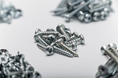 Self-tapping screws of various types are sorted into several piles. A photo with a shallow depth of field focusing on short round head screws.