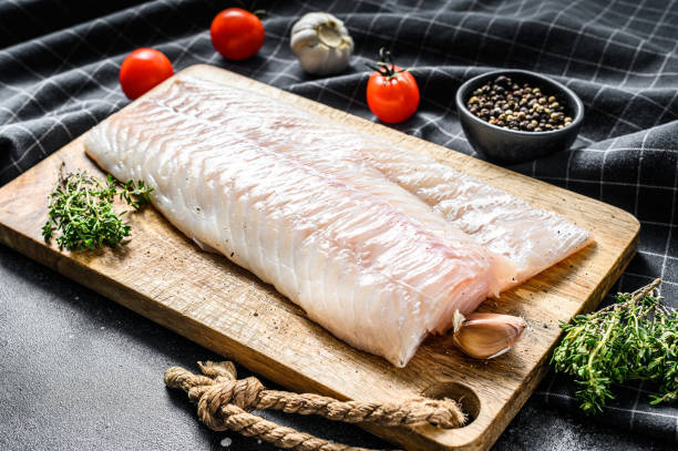 istock Raw cod fillet with and herbs on rustic wooden cutting board.  Black background. Top view 1278672805
