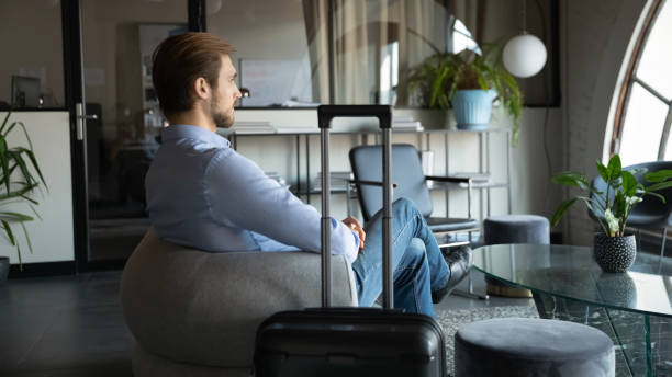 istock Side view pensive young man sitting with luggage at office. 1278673127