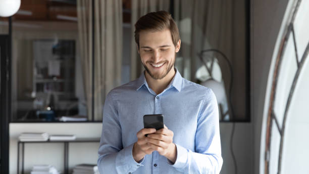 istock Smiling young businessman using phone in office. 1278673160