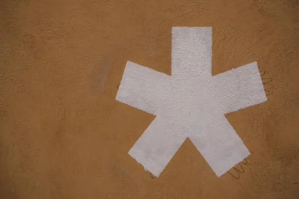 A Big, white Asterisk icon drawn on an light brown wall. Isolated. Close-up with copy space.