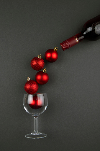 Glass with Christmas balls and wine bottle on black background