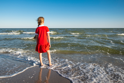Teenager Girl in a red dress running and having fun on the beach. Vacation or holiday concept