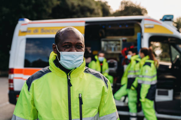Portrait of a male paramedic in front of an ambulance Portrait of a male paramedic in front of an ambulance. African ethnicity. He's wearing a protective face mask. ambulance photos stock pictures, royalty-free photos & images