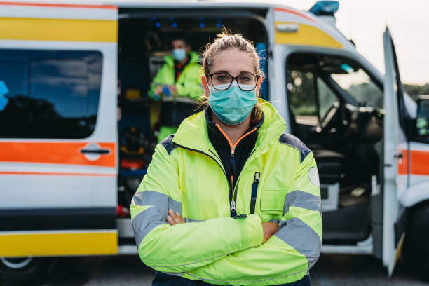 Portrait of a female paramedic in front of an ambulance outdoor Portrait of a female paramedic in front of an ambulance outdoor. She's wearing a protective face mask. frontline worker mask stock pictures, royalty-free photos & images