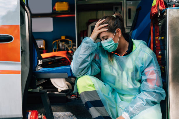 молодая женщина фельдшер грустно, сидя на машине скорой помощи - doctor tired protective workwear sadness стоковые фото и изображения