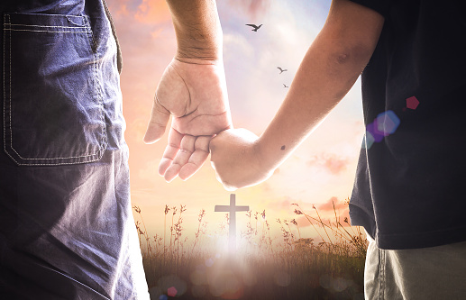 Father and son hold hands and stand in front of the cross
