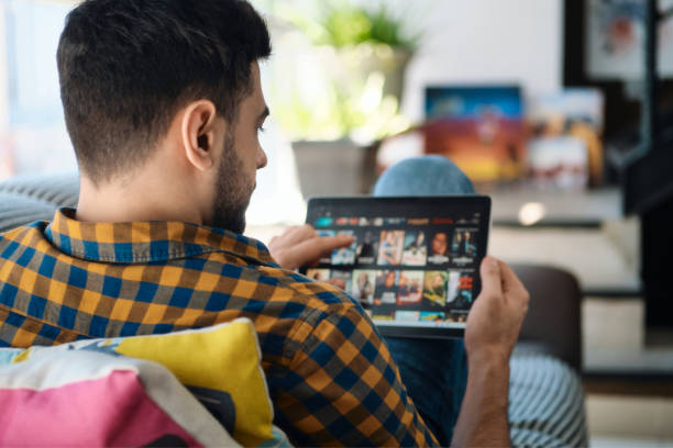 hombre eligiendo película para streaming en el ordenador de la tableta - descargando fotografías e imágenes de stock