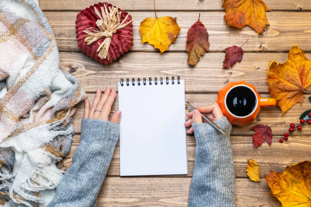 istock Desktop mock up planner. Top view composition with woman's hands in sweater, pumpkin styled cup of coffee and autumn themed decoration, fallen leaves on wooden background. Flat lay, copy space. 1278678316