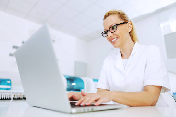 attractive smiling positive blond lab assistant sitting in laboratory and processing data. - smiling research science and technology clothing imagens e fotografias de stock