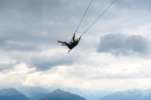 Kronplatz, Italy - August 28, 2020: A man enjoying a ride on a giant swing high above the alps on Kronplatz hiking & fun arena