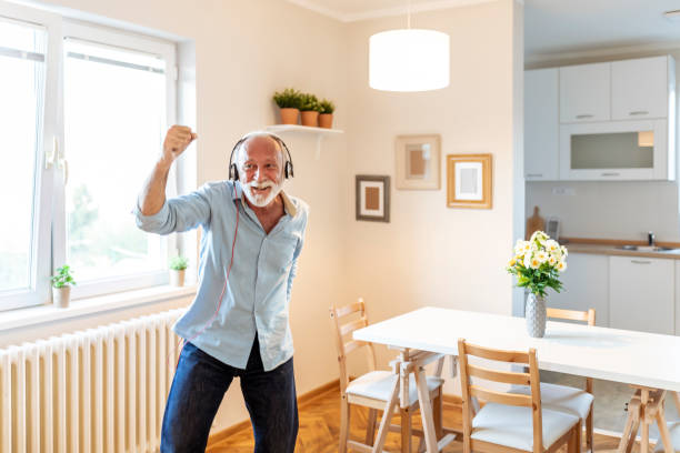 Young at heart Senior, happy, man listening to the music, with headphones on. Making happy gestures. Home interior. old person listening to radio stock pictures, royalty-free photos & images