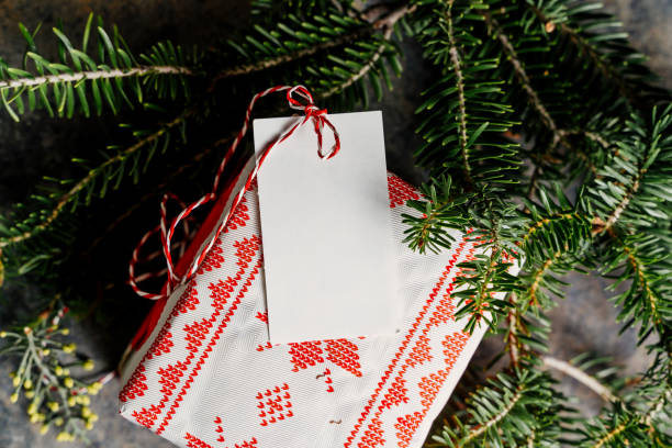 istock Wrapped christmas gift box, with empty tag and red tape, surrounded by pine branches on grunge blue background 1278692268