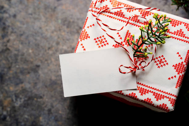 istock Wrapped christmas gift box, with empty tag and red tape, surrounded by pine branches on grunge blue background 1278692278