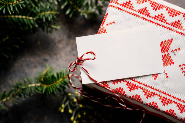 Wrapped christmas gift box, with empty tag and red tape, surrounded by pine branches on grunge blue background