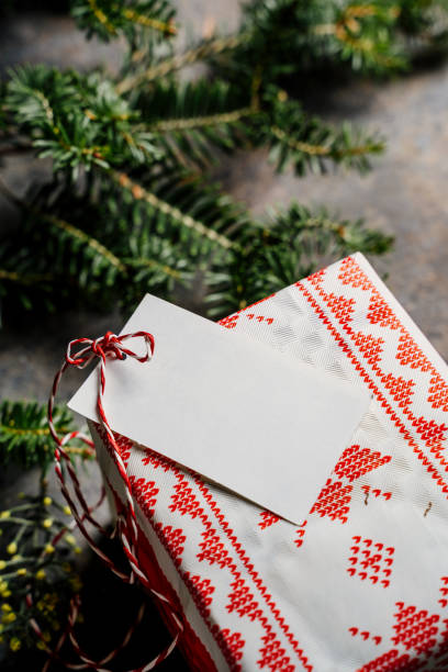 istock Wrapped christmas gift box, with empty tag and red tape, surrounded by pine branches on grunge blue background 1278692288
