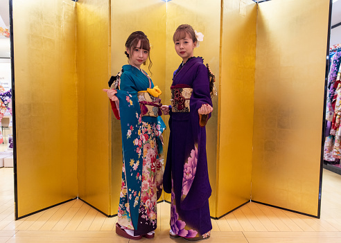 Full length portrait of young female friends in ‘Furisode’ kimono standing in front of golden ‘Byobu’ folding screen for ‘Seijin Shiki’ coming-of-age ceremony